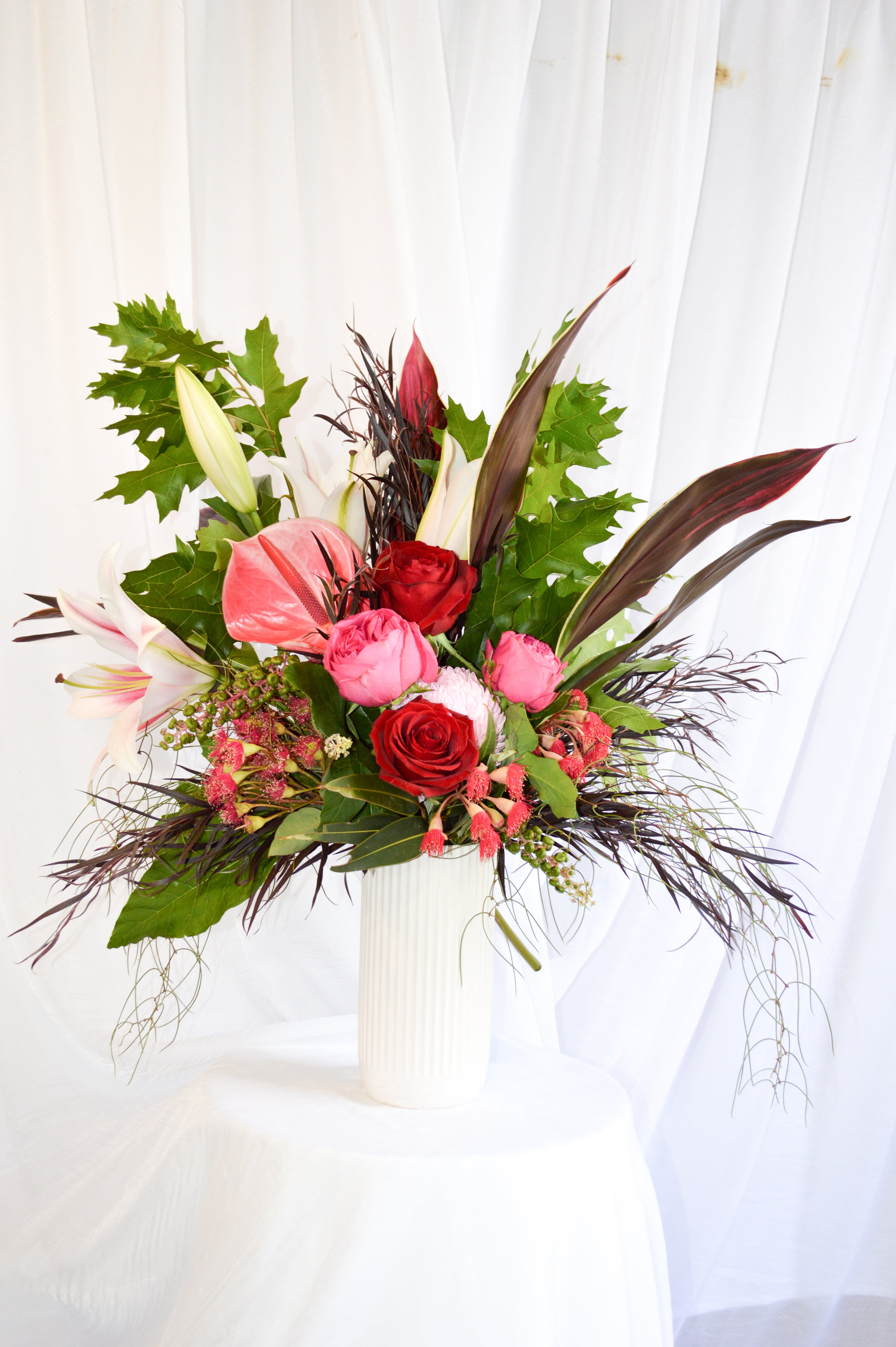 Pink and red bouquet featuring classic roses, lillies, and a mixture of funky foliage