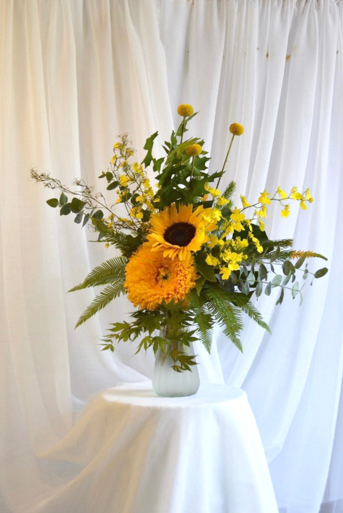Bright and cheery yellow themed bouquet featuring two types of sunflowers, yellow orchid, yellow billy buttons and greenery.